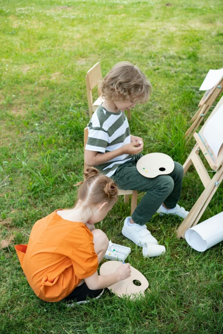 Two children painting outdoors, using palettes and easels for creative expression.